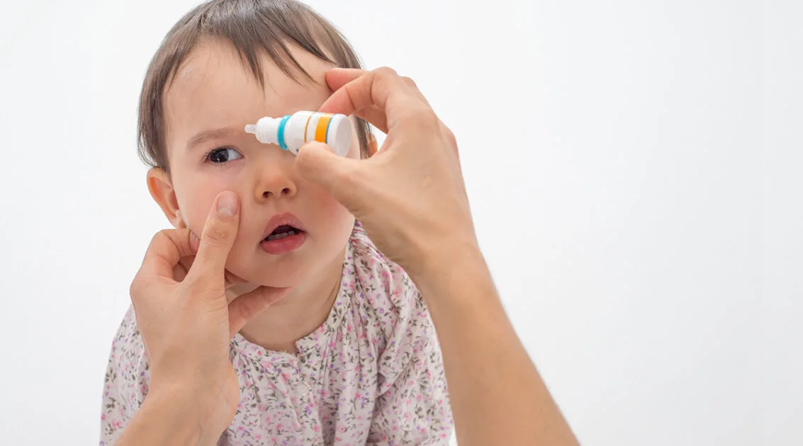 the picture is showing a child and someone is putting drops in his eyes 